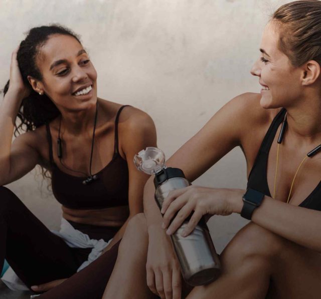 Two young women sitting and chatting after a workout, reflecting the joy and camaraderie of fitness friendship.