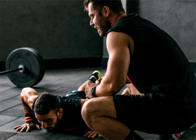 Man squatting down, providing encouragement to a friend during a workout, exemplifying support and motivation in fitness.