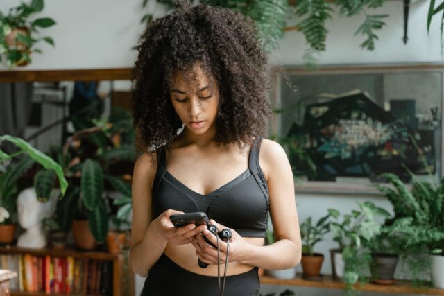 Image of a brown-skinned woman with curly hair holding a jump rope, looking at her phone for workout guidance