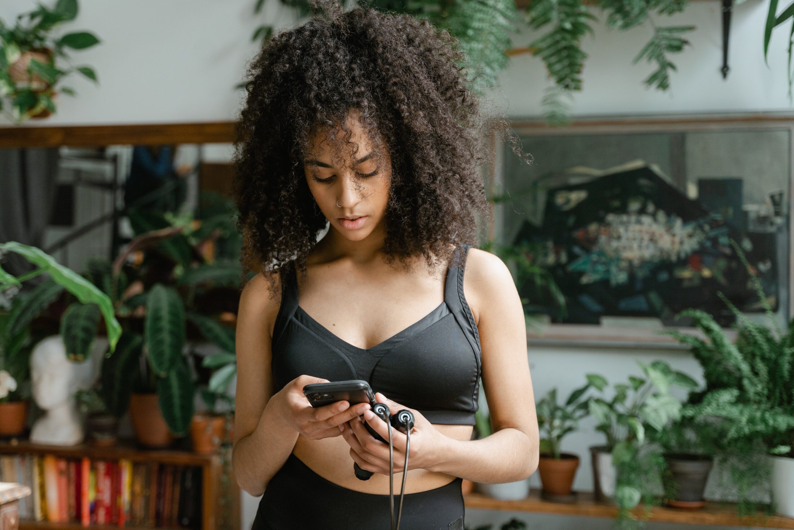 Image of a brown-skinned woman with curly hair holding a jump rope, looking at her phone for workout guidance