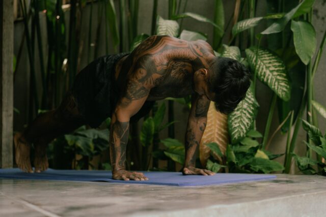 Photo of a fit man with tattoos confidently holding a bodyweight plank, showcasing strength and stability in his core workout.
