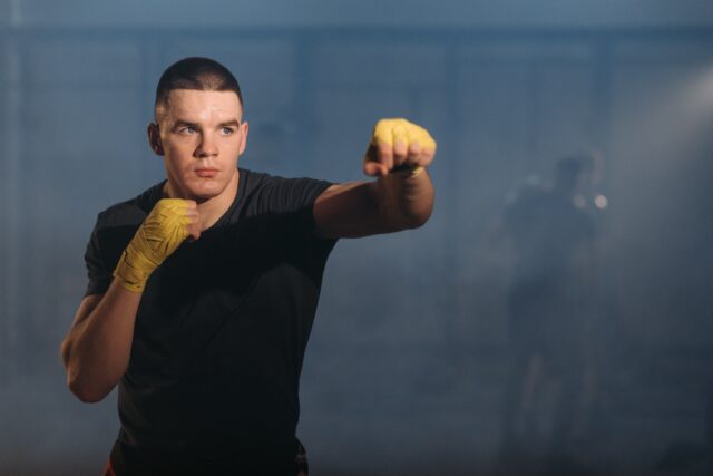 A man in a black shirt with yellow boxing hand wraps engaged in shadow boxing, showcasing skill and focus in his training.