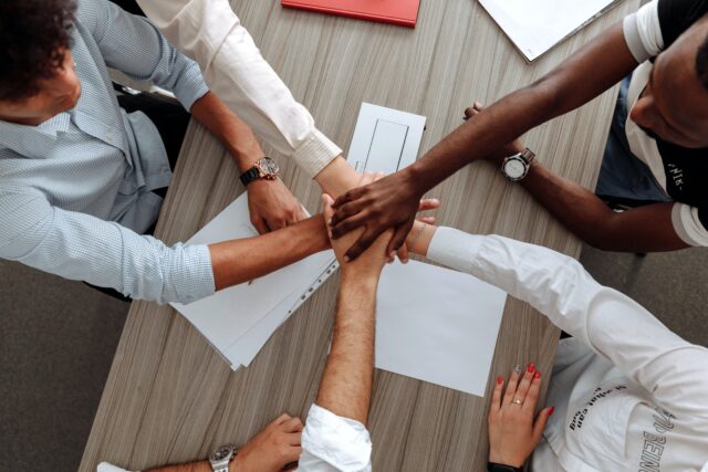 A group of corporate employees bring their hands together in solidarity 