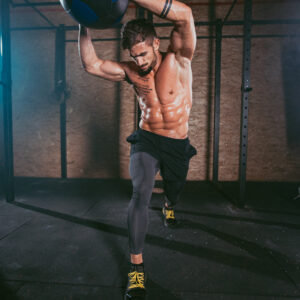 Details of a athletic guy using a cross fit ball to do his hard training workout exercises in a dark gym class.
