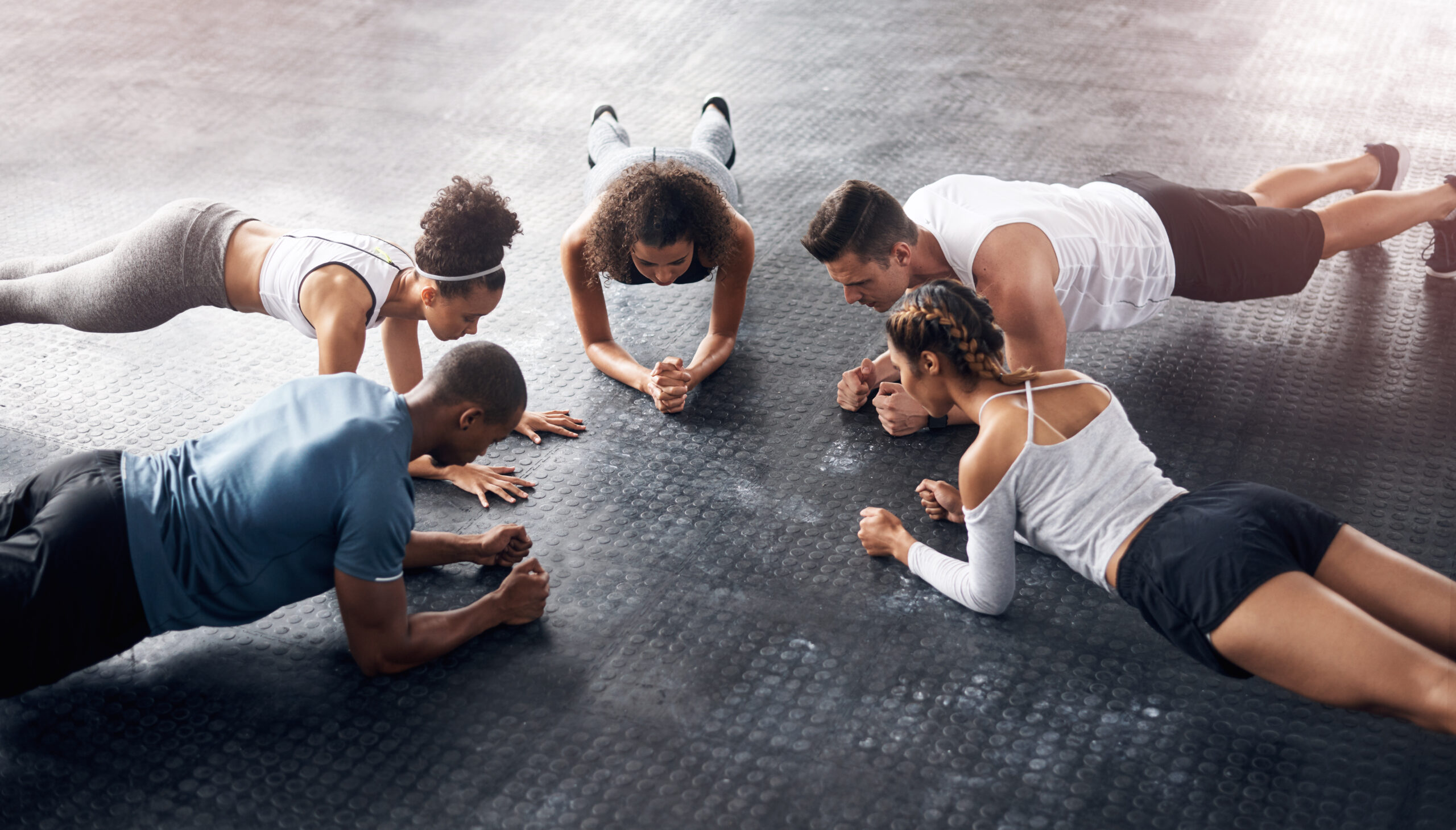 Class, fitness and plank in group at gym for workout, core exercise or training together indoors. Diverse people, friends and warm up for ab muscle, session and sport for health on gymnasium floor.